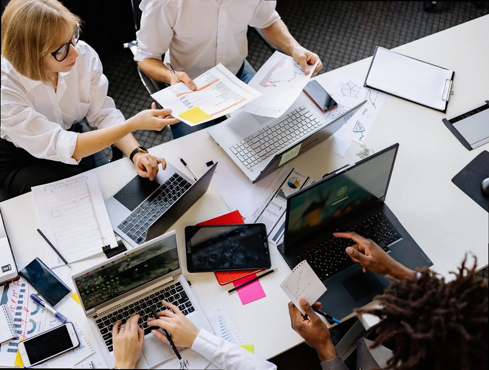 Top view of a diverse work team engaged in a collaborative office meeting, discussing papers and using laptops.